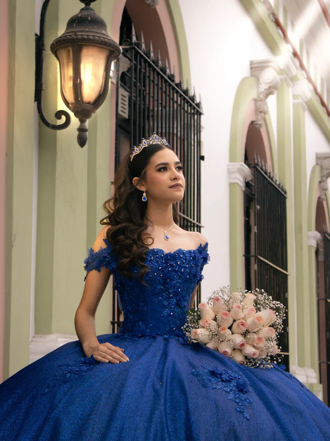Quinceañera con vestido azul rey y bouquet de rosas bajo farol