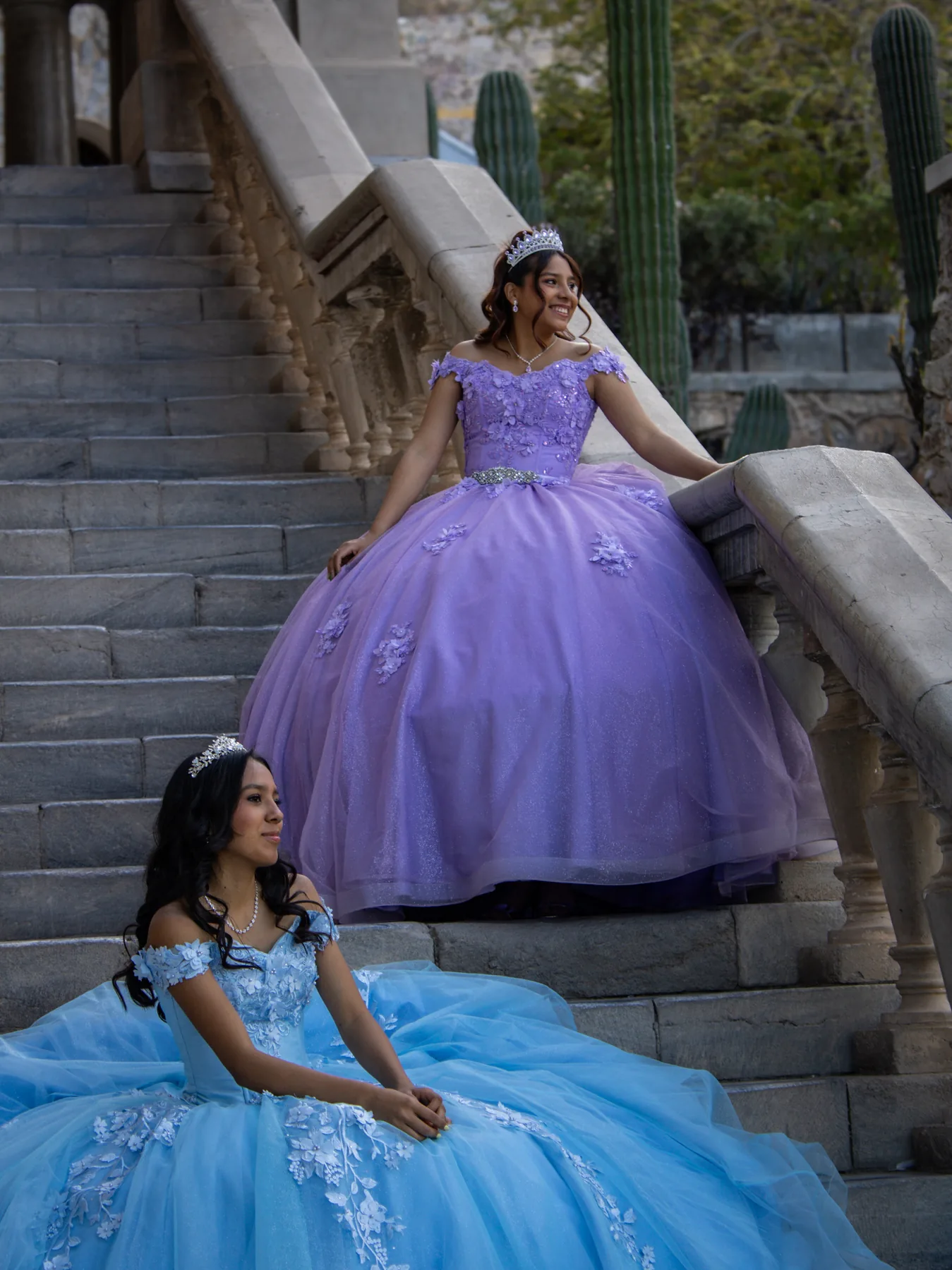 Dos quinceañeras con vestidos lavanda y azul en escalinata de cantera